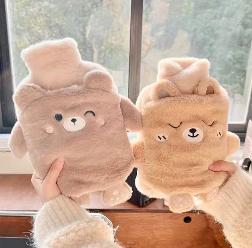 Deux bouillottes peluche en forme d’ours, beige et rose, tenues devant une fenêtre